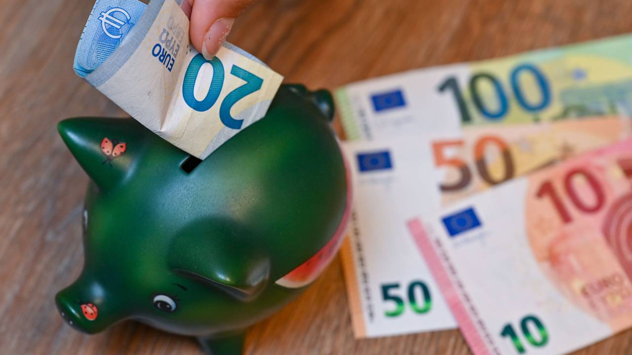 Ein Mädchen steckt einen 20-Euro-Schein in ein Sparschwein.