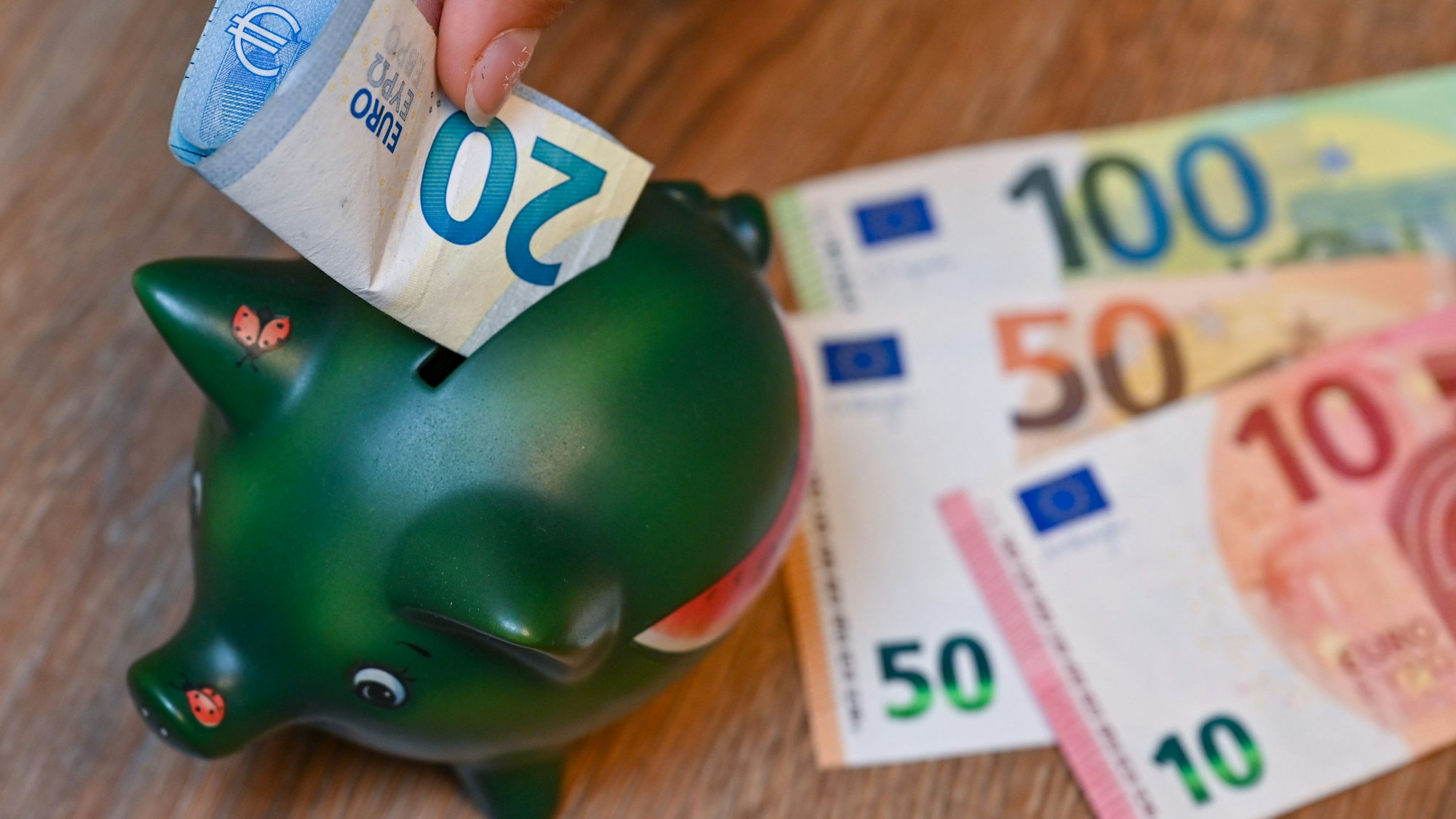 Ein Mädchen steckt einen 20-Euro-Schein in ein Sparschwein.