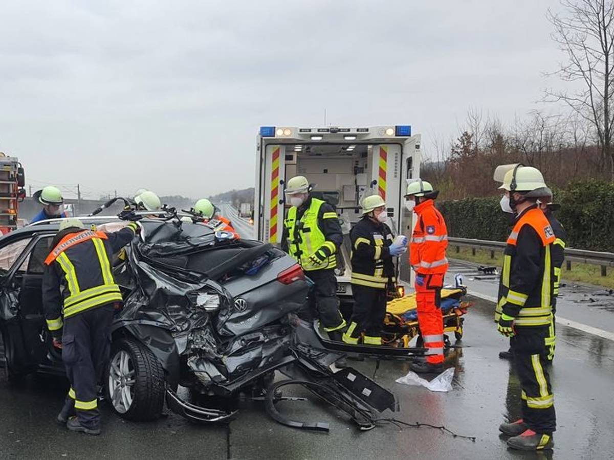 Einsatzkräfte der Feuerwehr stehen an einem zerfetzten Fahrzeug.