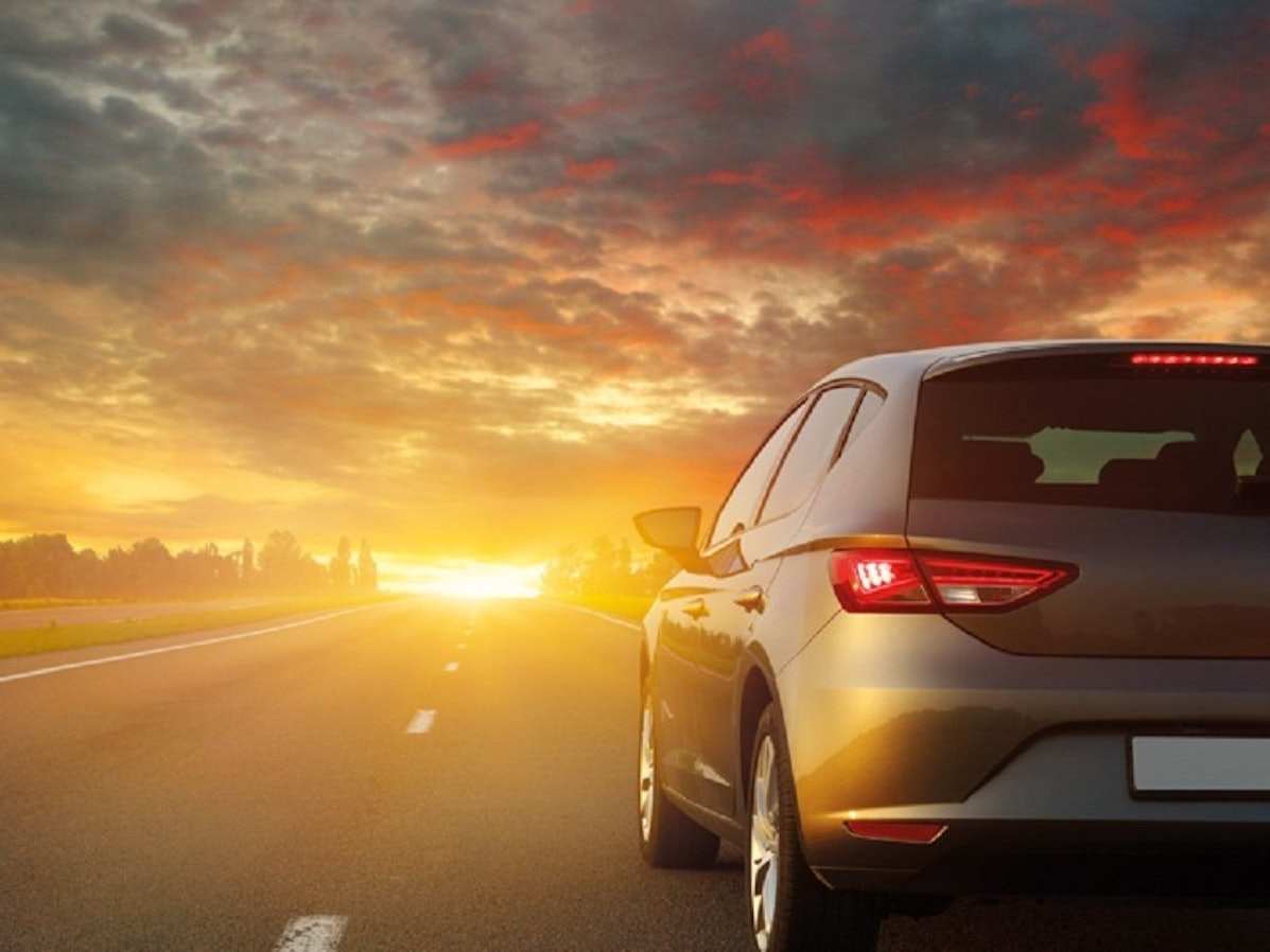 Ein Auto der ADAC-Autovermietung fährt über eine Landstraße in Richtung Sonnenuntergang.