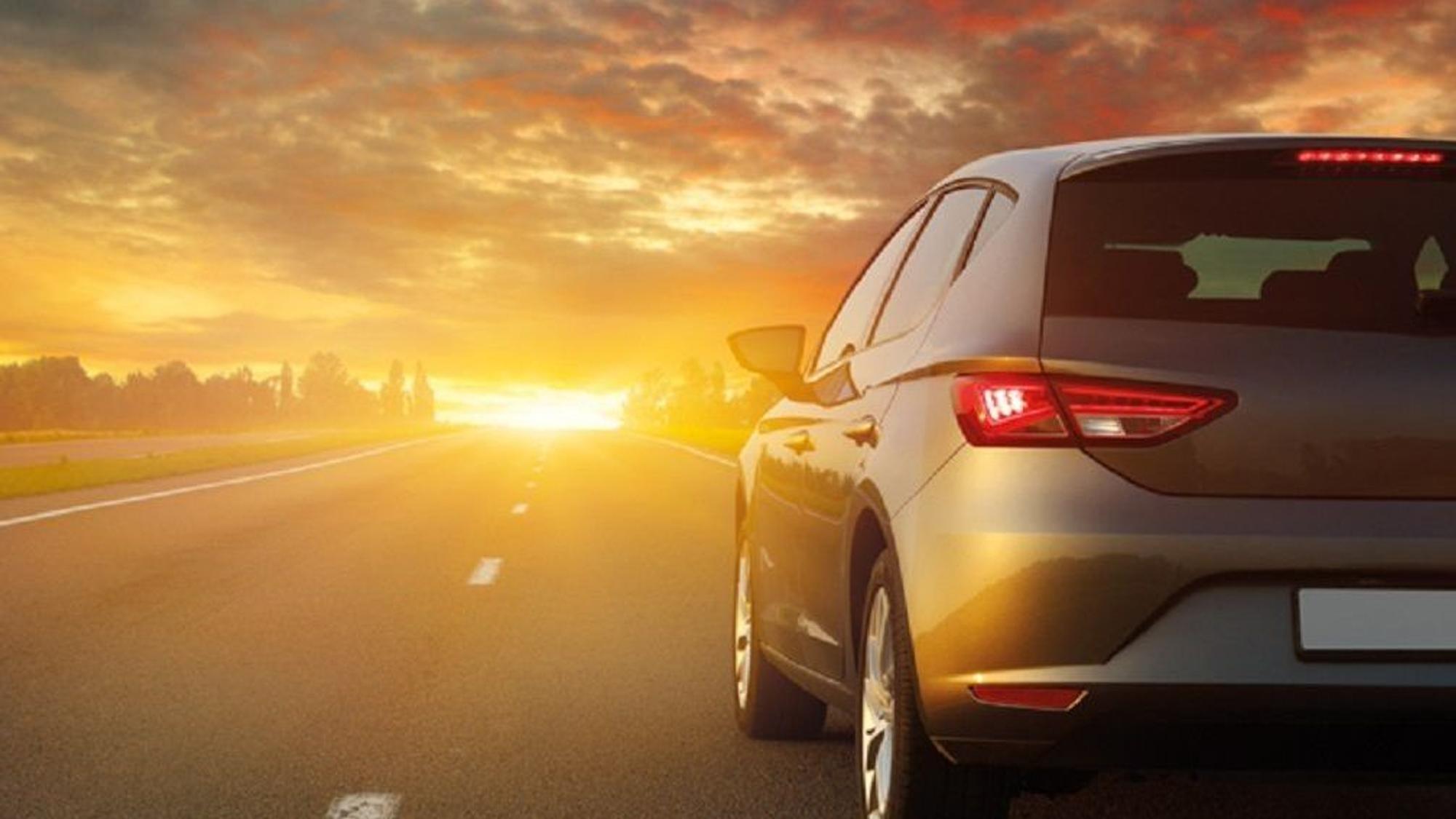 Ein Auto der ADAC-Autovermietung fährt über eine Landstraße in Richtung Sonnenuntergang.