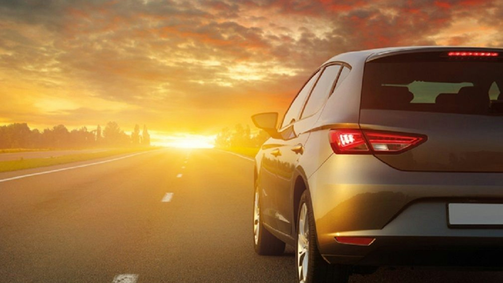 Ein Auto der ADAC-Autovermietung fährt über eine Landstraße in Richtung Sonnenuntergang.