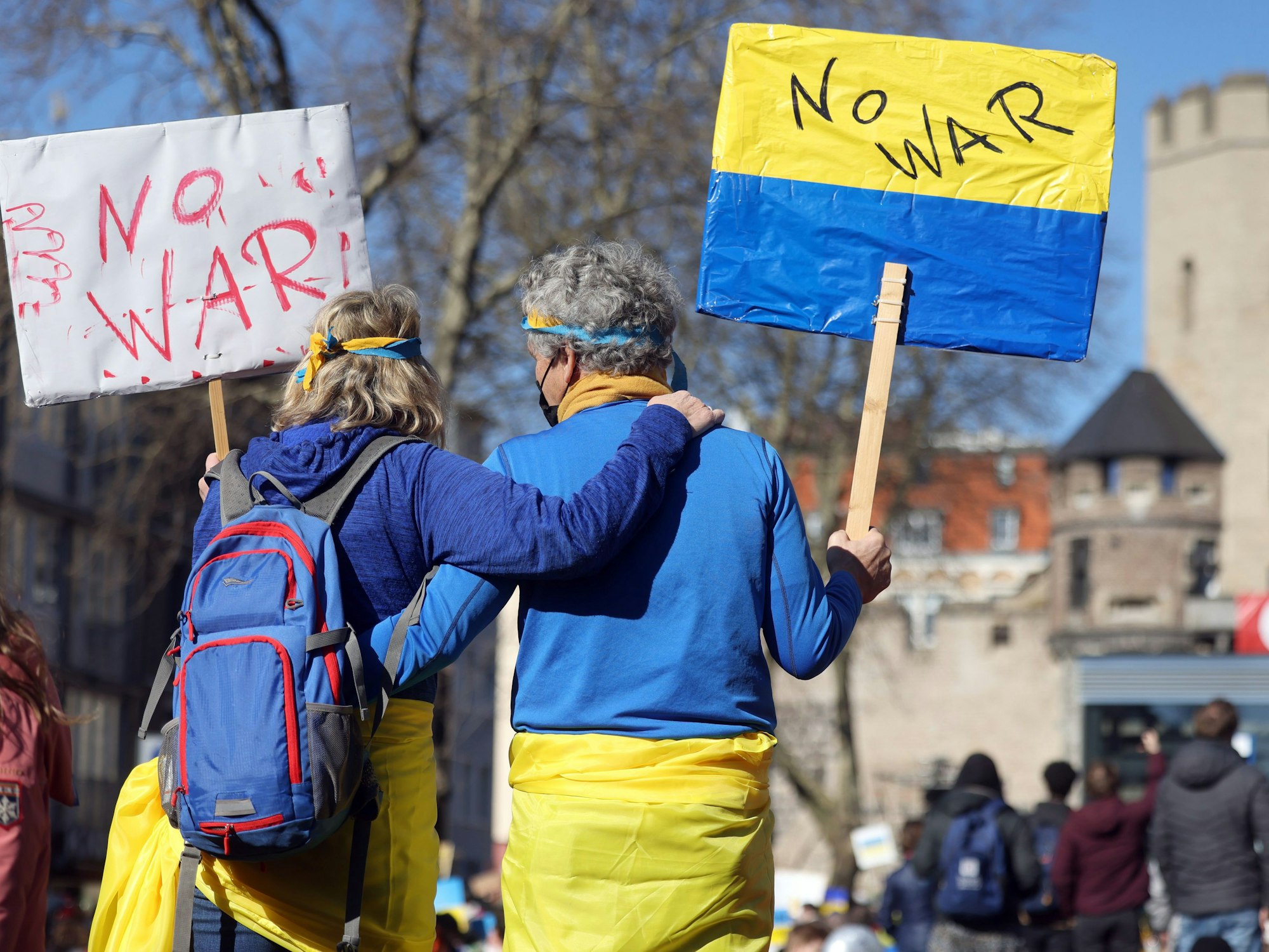 Mann und Frau zeigen blau-gelbe Schilder mit der Aufschrift „No War“ auf einer Friedensdemo in Köln.