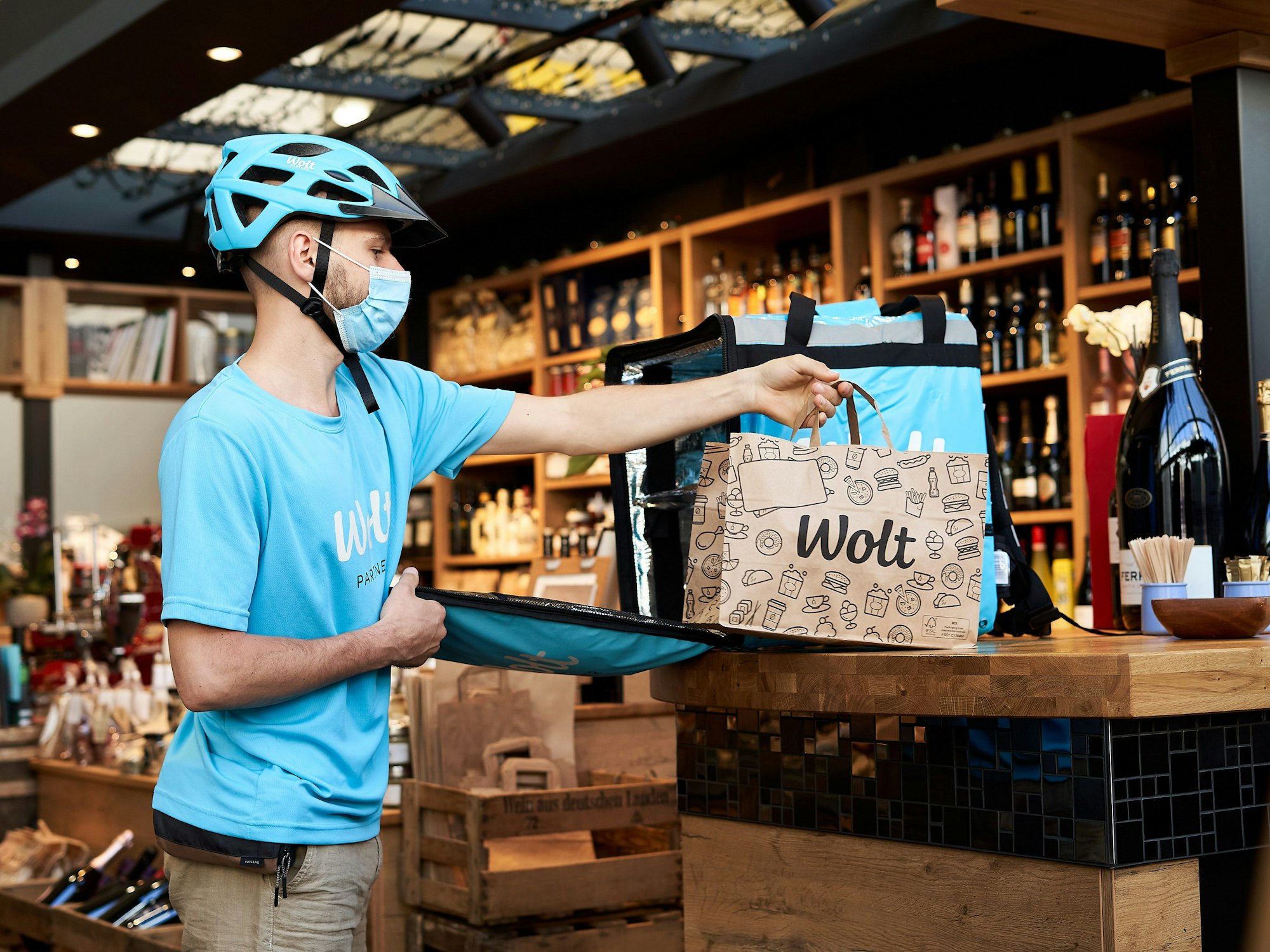 Ein Kurier des Lieferdienstes Wolt legt eine Tüte mit den Bestellungen auf einen Tisch.