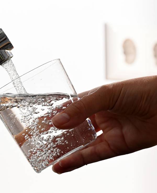 Eine Hand hält ein Wasserglas unter einen Wasserhahn.