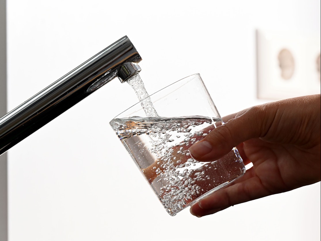 Eine Hand hält ein Wasserglas unter einen Wasserhahn.