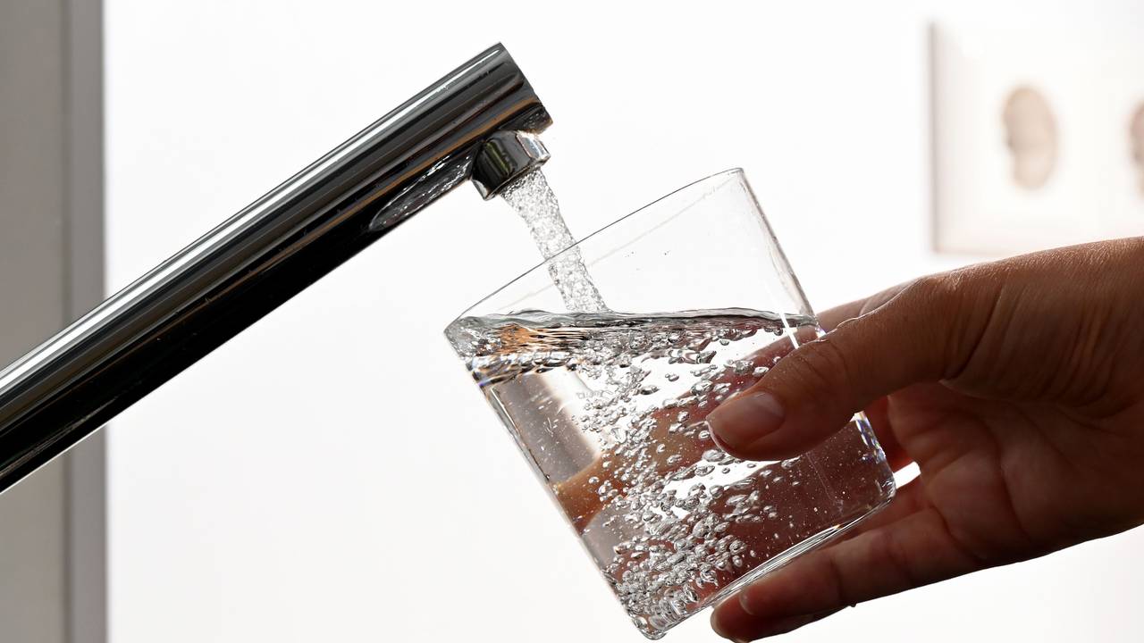 Eine Hand hält ein Wasserglas unter einen Wasserhahn.