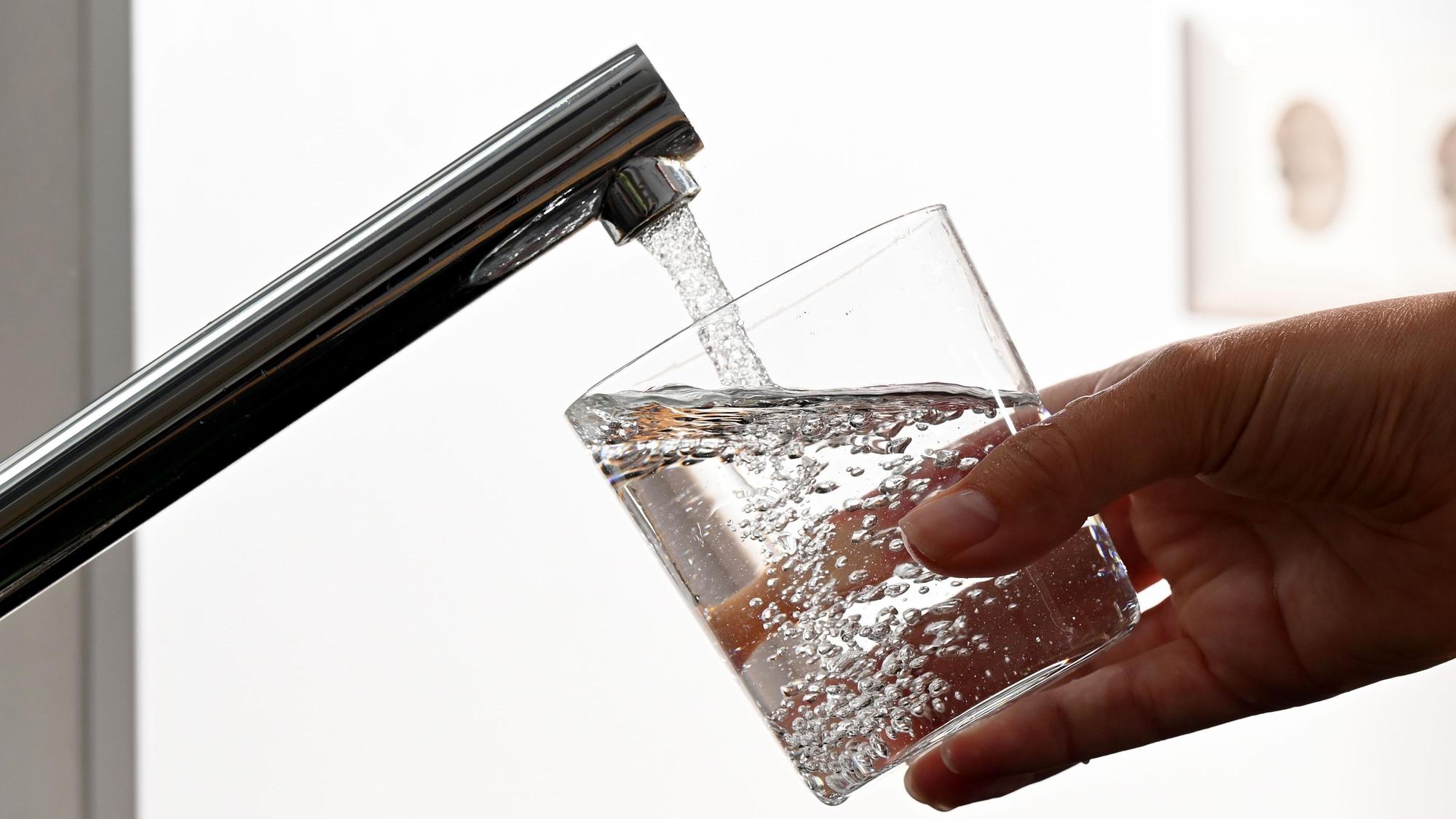 Eine Hand hält ein Wasserglas unter einen Wasserhahn.