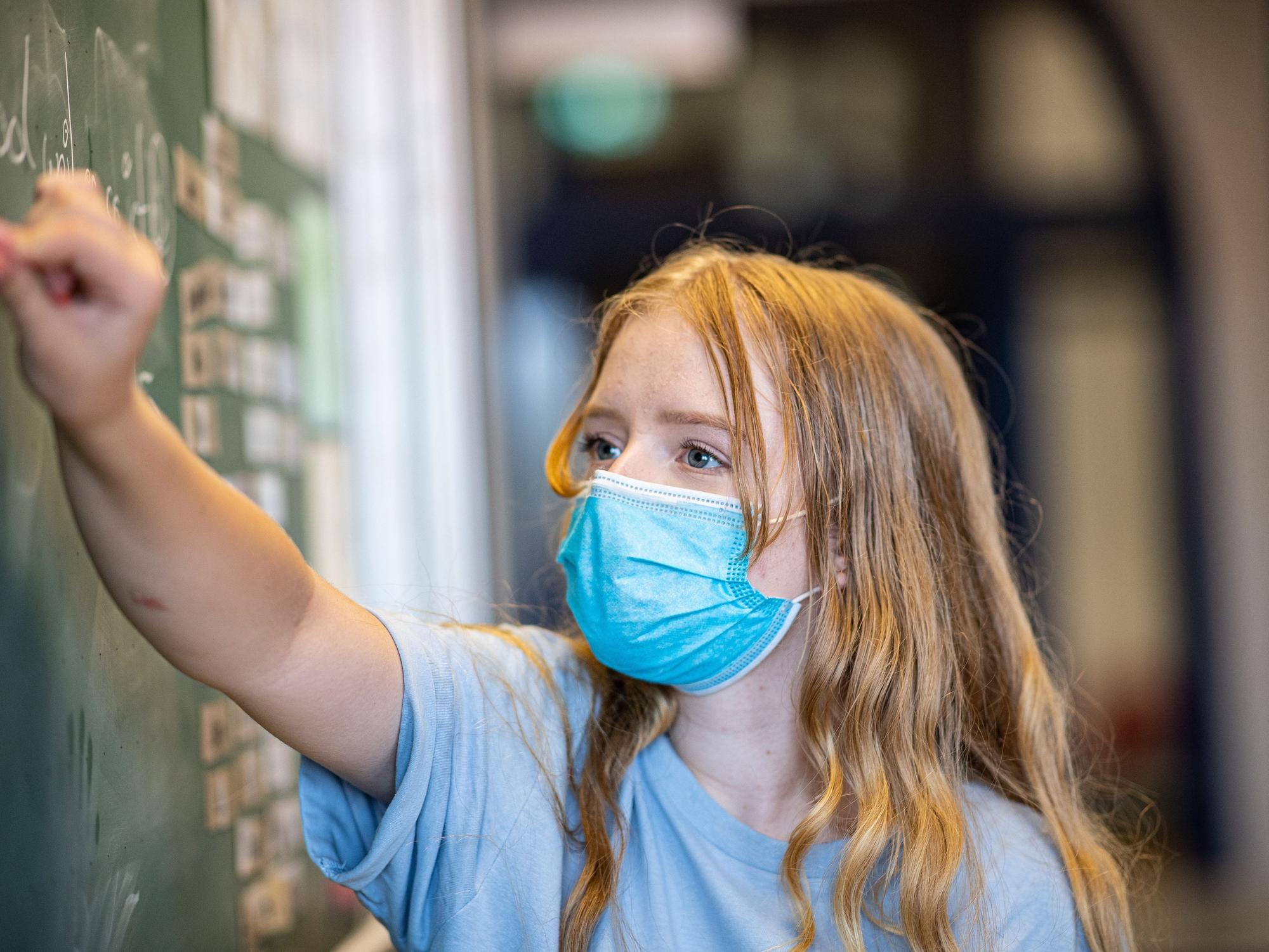 Eine Schülerin einer Gesamtschule steht mit einer Mund- und Nasenmaske vor einer Tafel. Zum 2. April 2022 fällt die Maskenpflicht an den Schulen in Nordrhein-Westfalen weg.