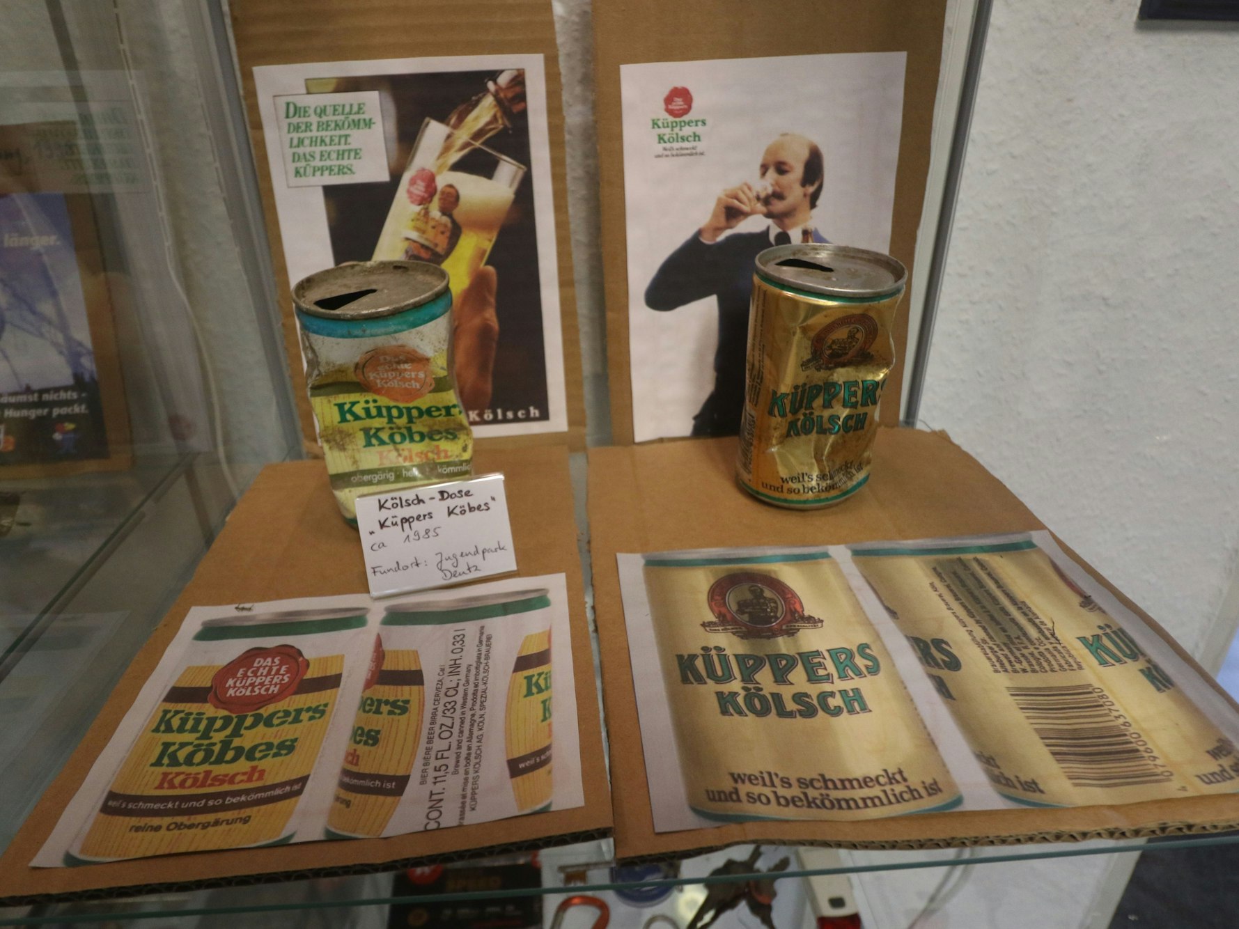Zwei Bierdosen stehen in einer Vitrine.