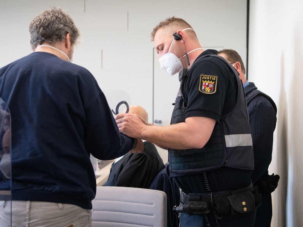 21.03.2022, Rheinland-Pfalz, Bad Kreuznach: Der Angeklagte wird in Handschellen in den Gerichtssaal gebracht. Der Mann soll im vergangenen Jahr in Bad Kreuznach den Mitarbeiter einer Tankstelle erschossen haben, nachdem dieser ihn auf die coronabedingte Maskenpflicht hingewiesen hatte.