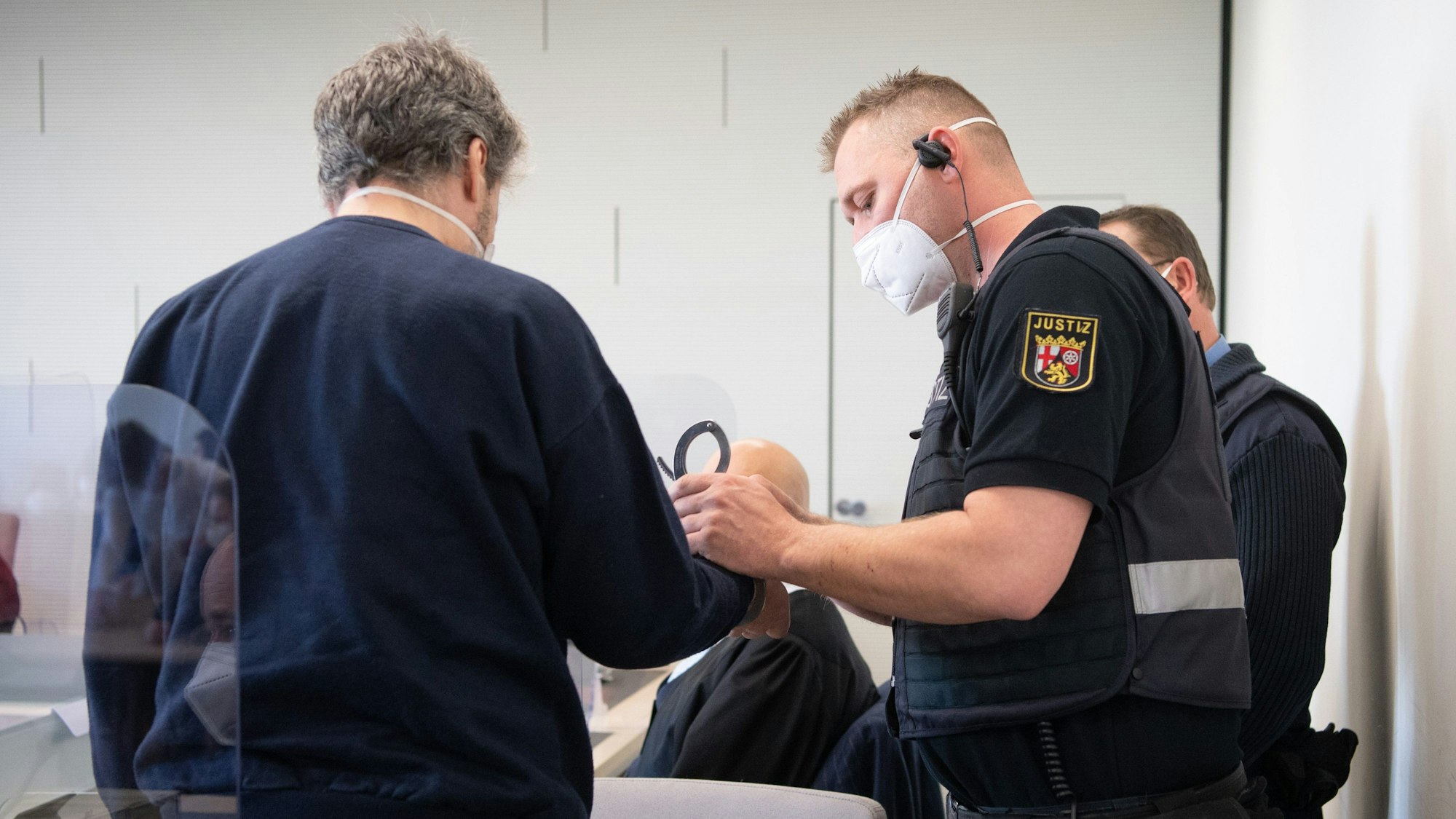 21.03.2022, Rheinland-Pfalz, Bad Kreuznach: Der Angeklagte wird in Handschellen in den Gerichtssaal gebracht. Der Mann soll im vergangenen Jahr in Bad Kreuznach den Mitarbeiter einer Tankstelle erschossen haben, nachdem dieser ihn auf die coronabedingte Maskenpflicht hingewiesen hatte.