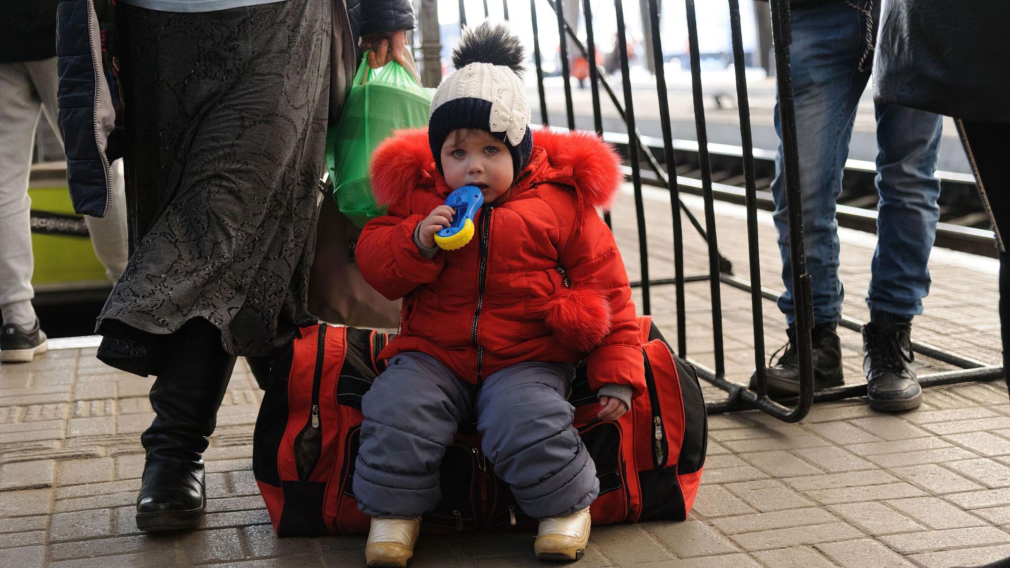 Ein Kind sitzt auf einem Gepäckstück am Bahnhof von Lwiw.
