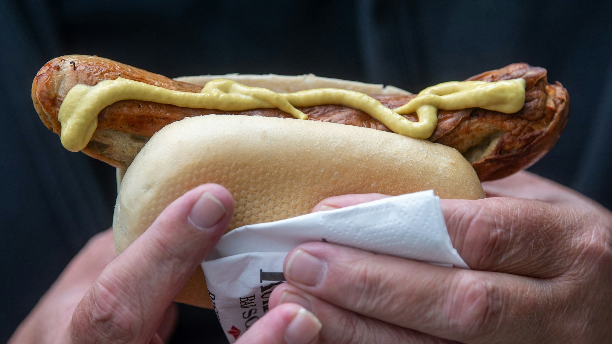 Ein Mann hält eine Bratwurst mit Senf in der Hand.