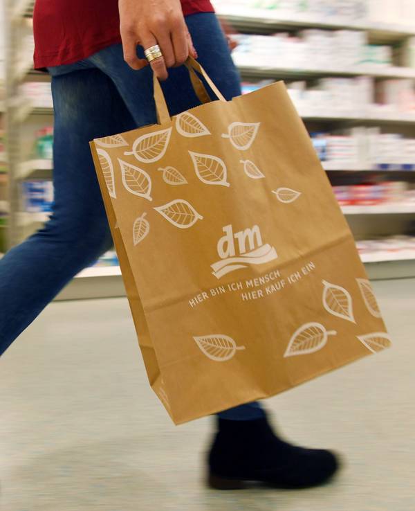 Eine Person geht in einer Filiale der Drogeriemarktkette dm mit einer dm-Tasche durch das Geschäft.