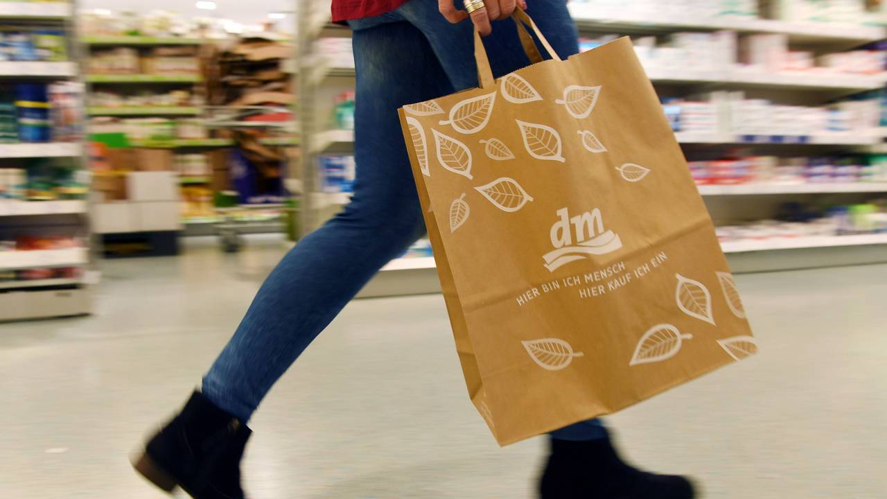 Eine Person geht in einer Filiale der Drogeriemarktkette dm mit einer dm-Tasche durch das Geschäft.