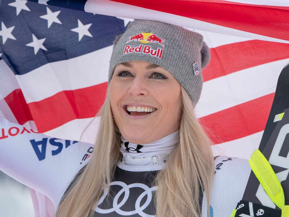 Lindsey Vonn hält amerikanische Flagge hoch und lächelt.