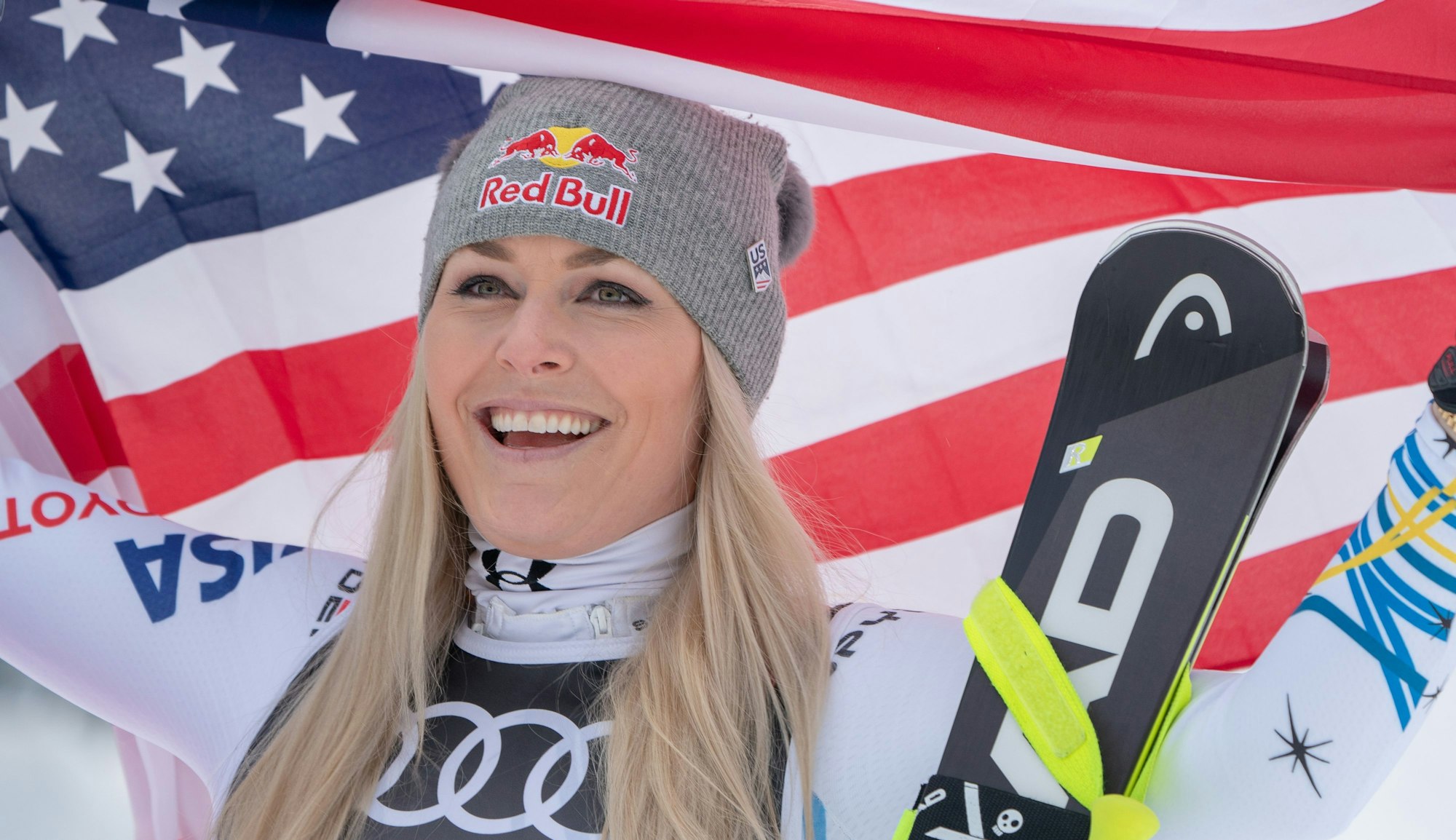 Lindsey Vonn hält amerikanische Flagge hoch und lächelt.
