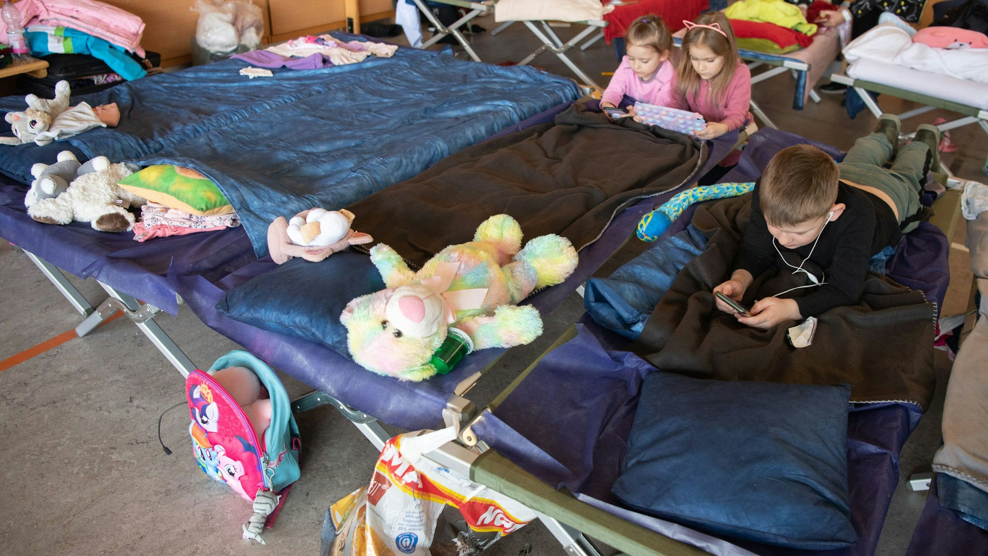 Geflüchtete Kinder aus der Ukraine liegen in der Notunterkunft auf ihren Feldbetten und vertreiben sich die Zeit.