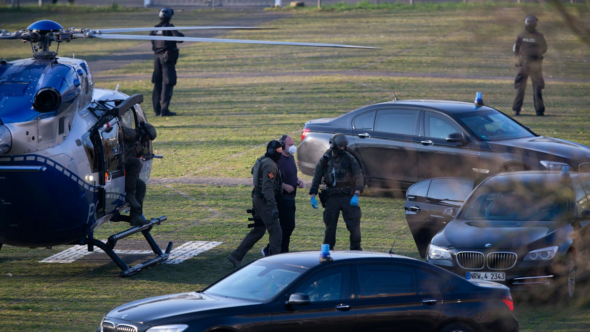 Der Angeklagte Thomas Drach kommt mit dem Hubschrauber auf dem Gelände des Justizzentrums Köln an und wird von zwei vermummten Polizisten begleitet.