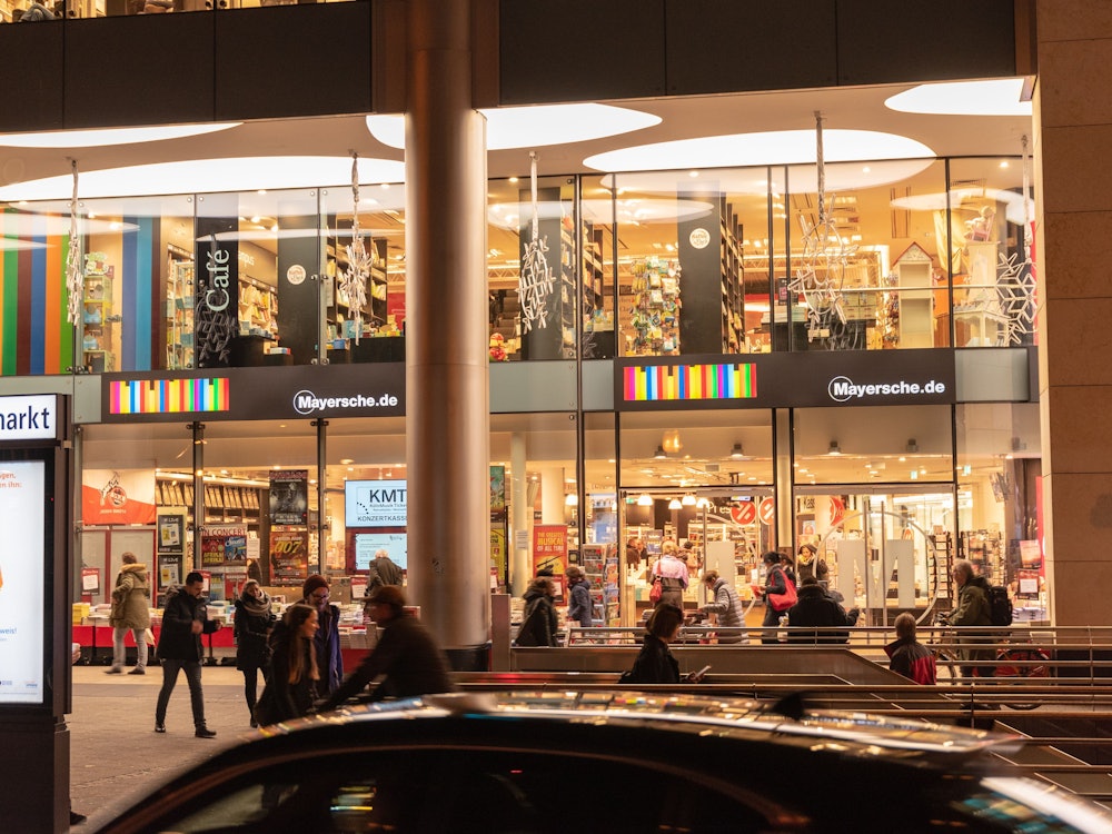 Die Mayersche Buchhandlung am Kölner Neumarkt hell erleuchtet in den Abendstunden.