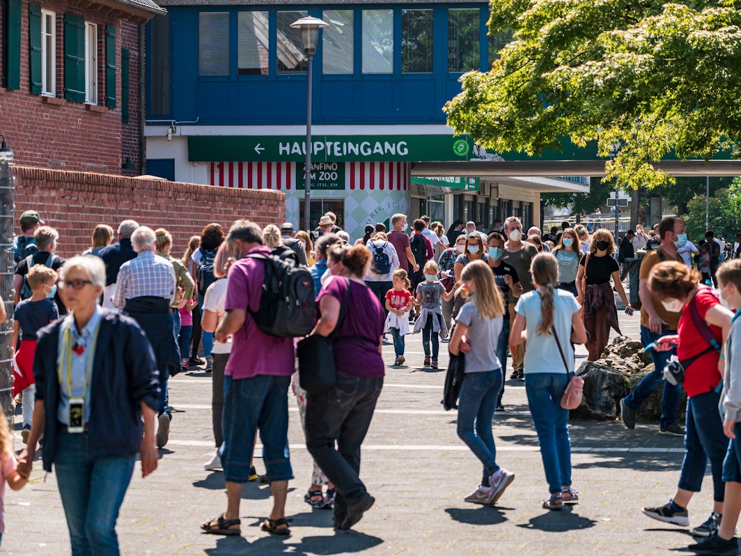 Menschen gehen bei Sonnenschein am Kölner Zoo vorbei.