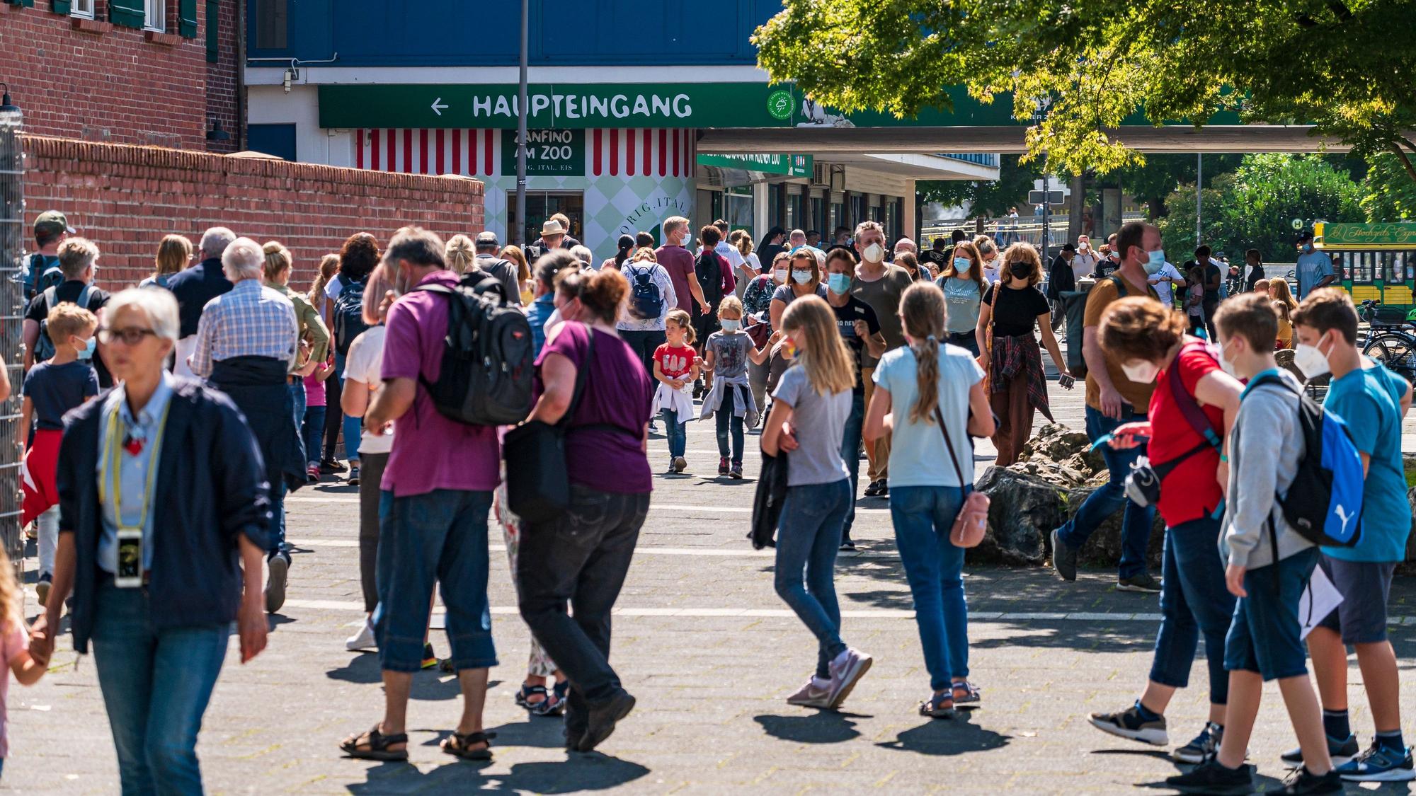 Menschen gehen bei Sonnenschein am Kölner Zoo vorbei.