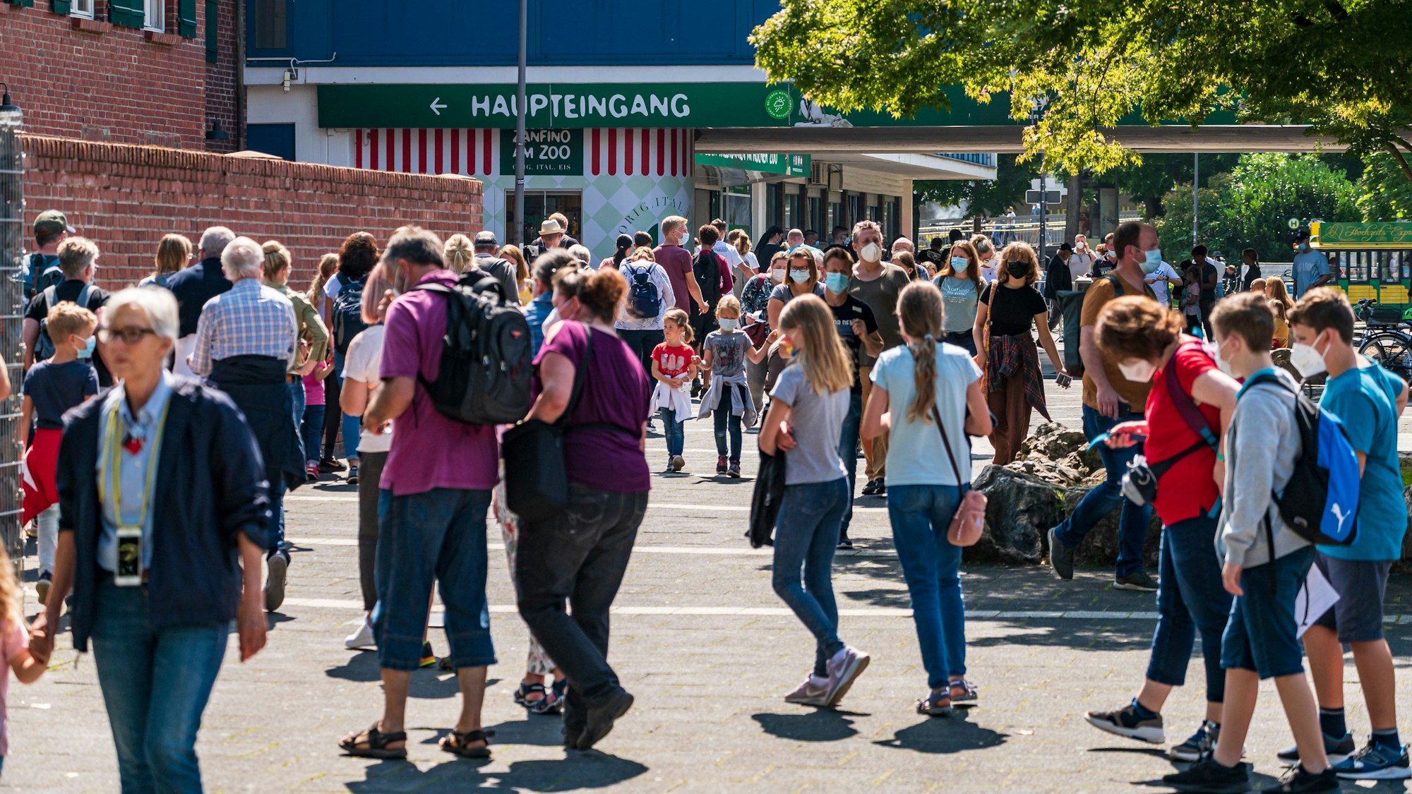Menschen gehen bei Sonnenschein am Kölner Zoo vorbei.