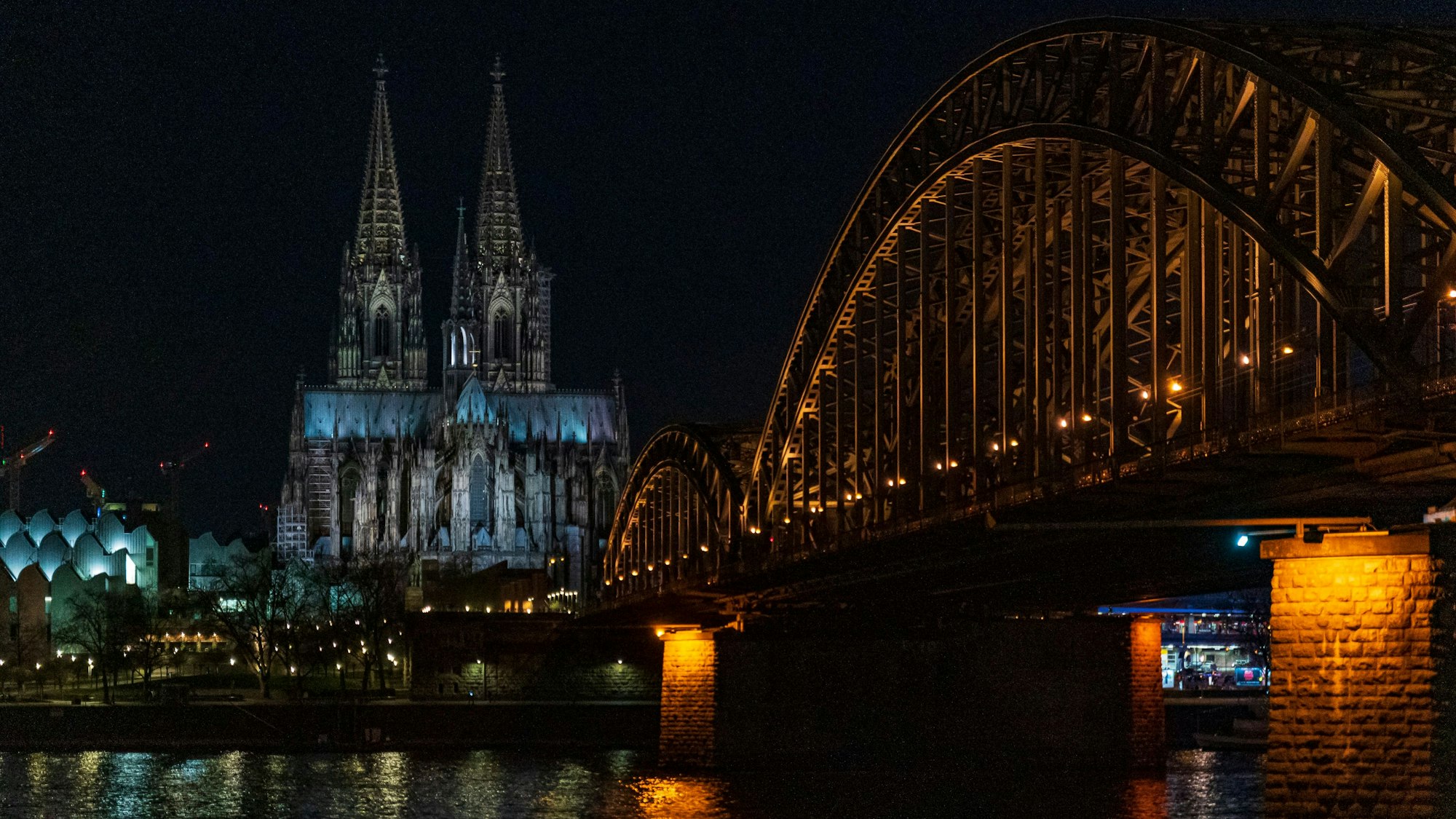 Der Kölner Dom liegt im Dunkeln, auch eine Rheinbrücke im Vordergrund ist nicht hell beleuchtet.