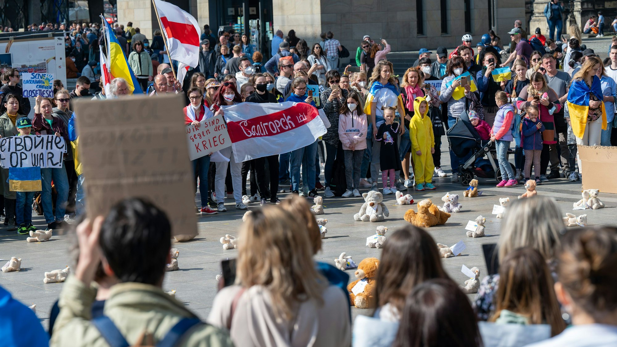 Teilnehmer der Kundgebung stehen um den Platz herum, auf dem die Teddys niedergelegt wurden.