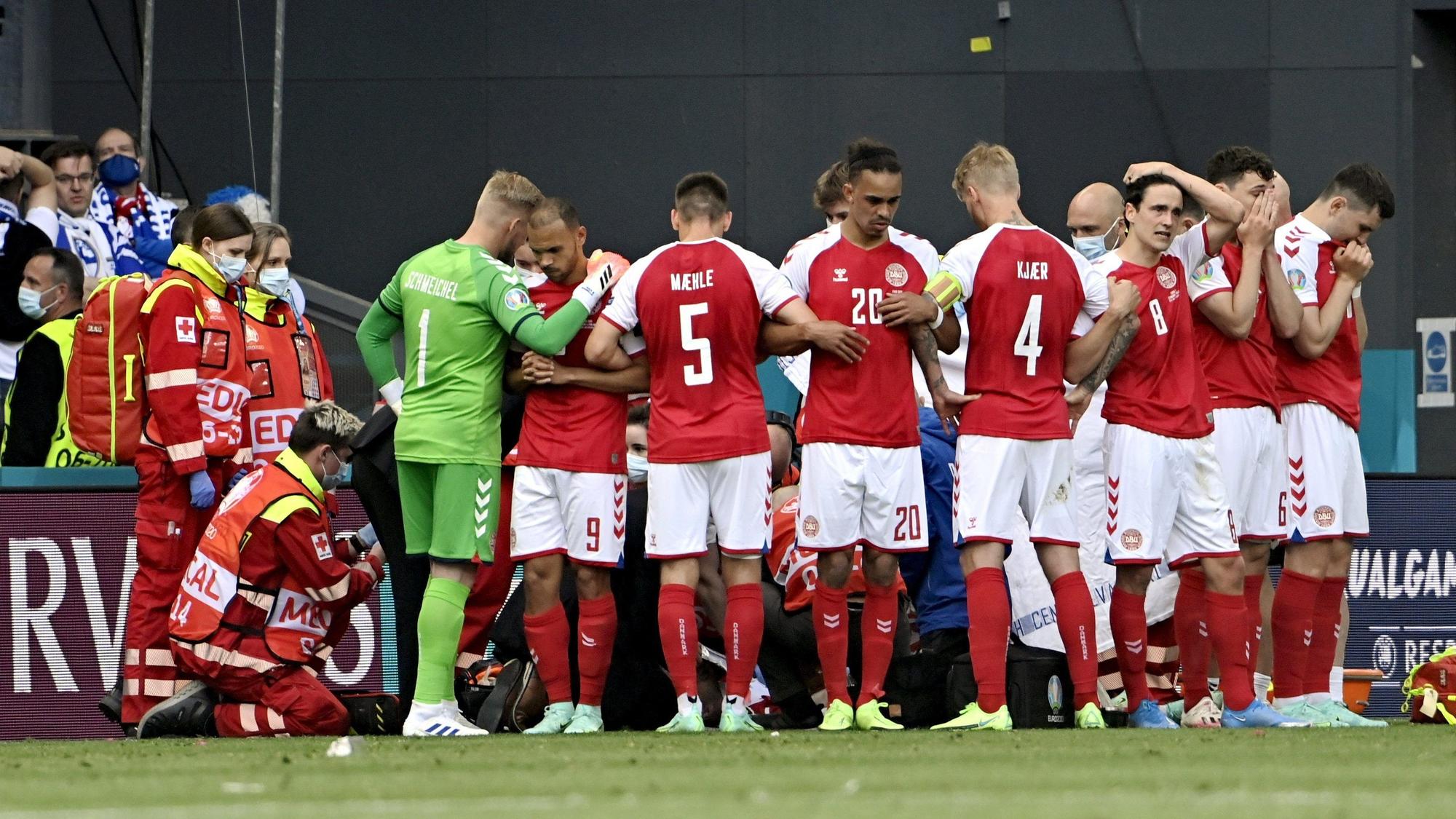 Christian Eriksen von Dänemark (auf dem Boden) wird medizinisch behandelt, seine Teamkollegen bilden einen Sicht-Wall