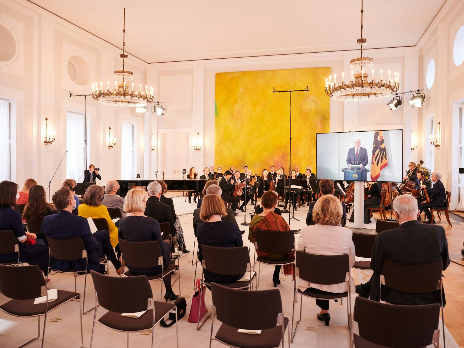 Die Berliner Philharmoniker sitzen am 27. März 2022 im Schloss Bellevue vor ein paar Dutzend Zuschauern, während Bundespräsident Frank-Walter Steinmeier wegen Krankheit per Video zugeschaltet ist. Er spricht vor dem Konzert „Für Freiheit und Frieden. Ein Konzert der Berliner Philharmoniker im Schloss Bellevue“.