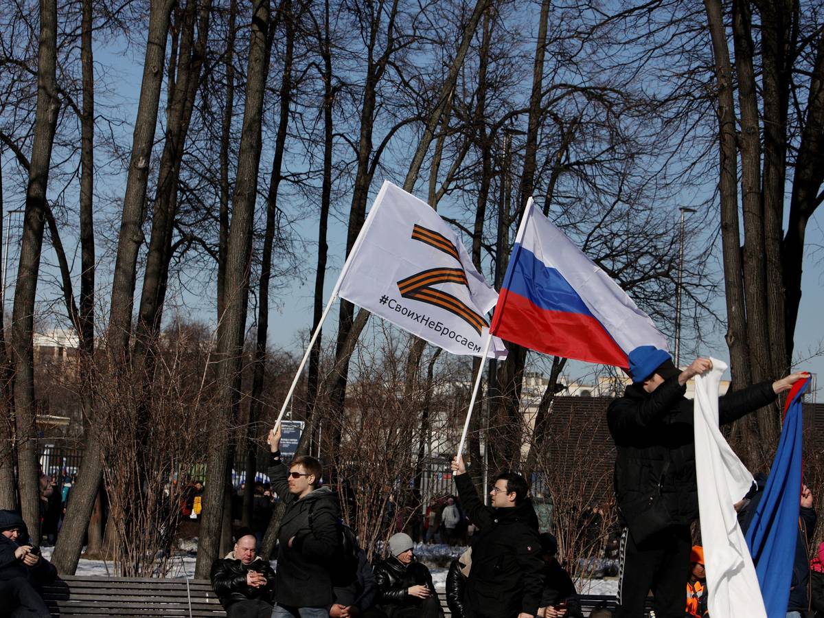 Russische Männer halten Fahnen mit der Nationalflagge und dem Kriegssymbol Z hoch.