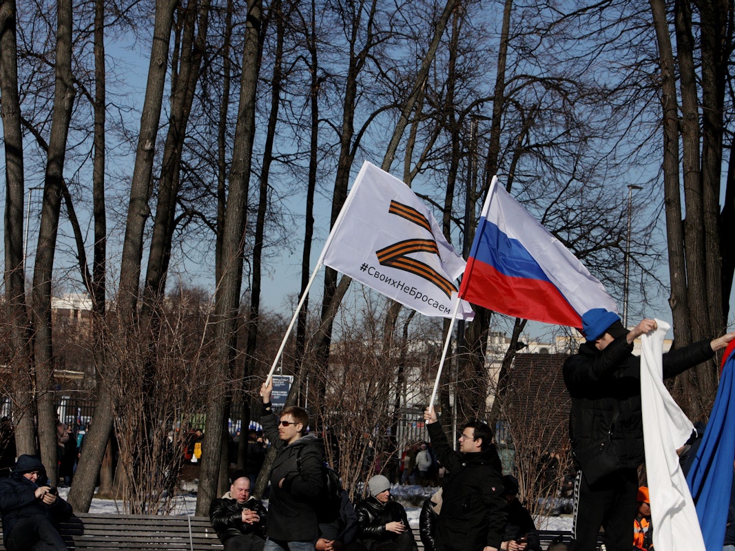 Russische Männer halten Fahnen mit der Nationalflagge und dem Kriegssymbol Z hoch.