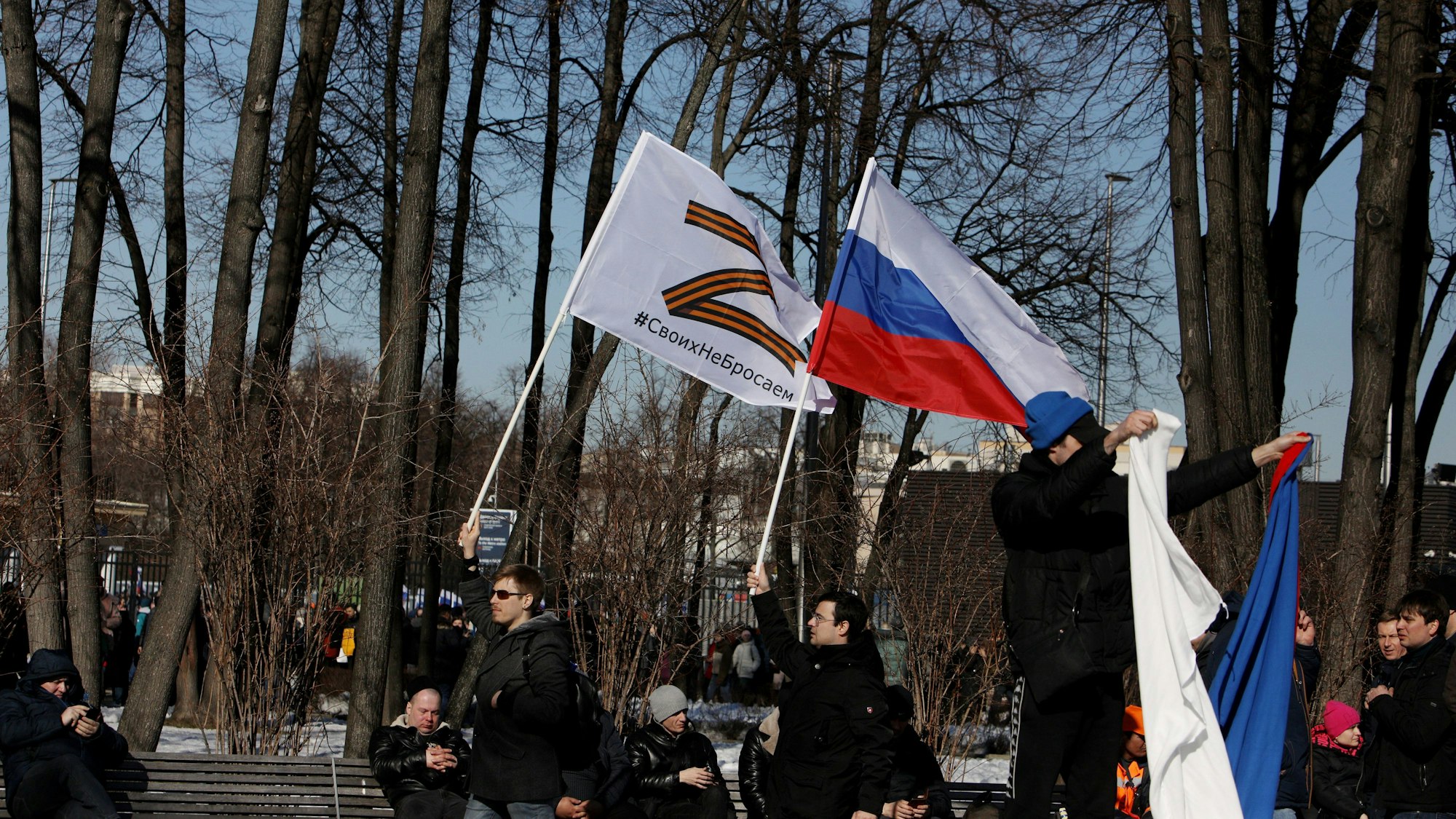 Russische Männer halten Fahnen mit der Nationalflagge und dem Kriegssymbol Z hoch.