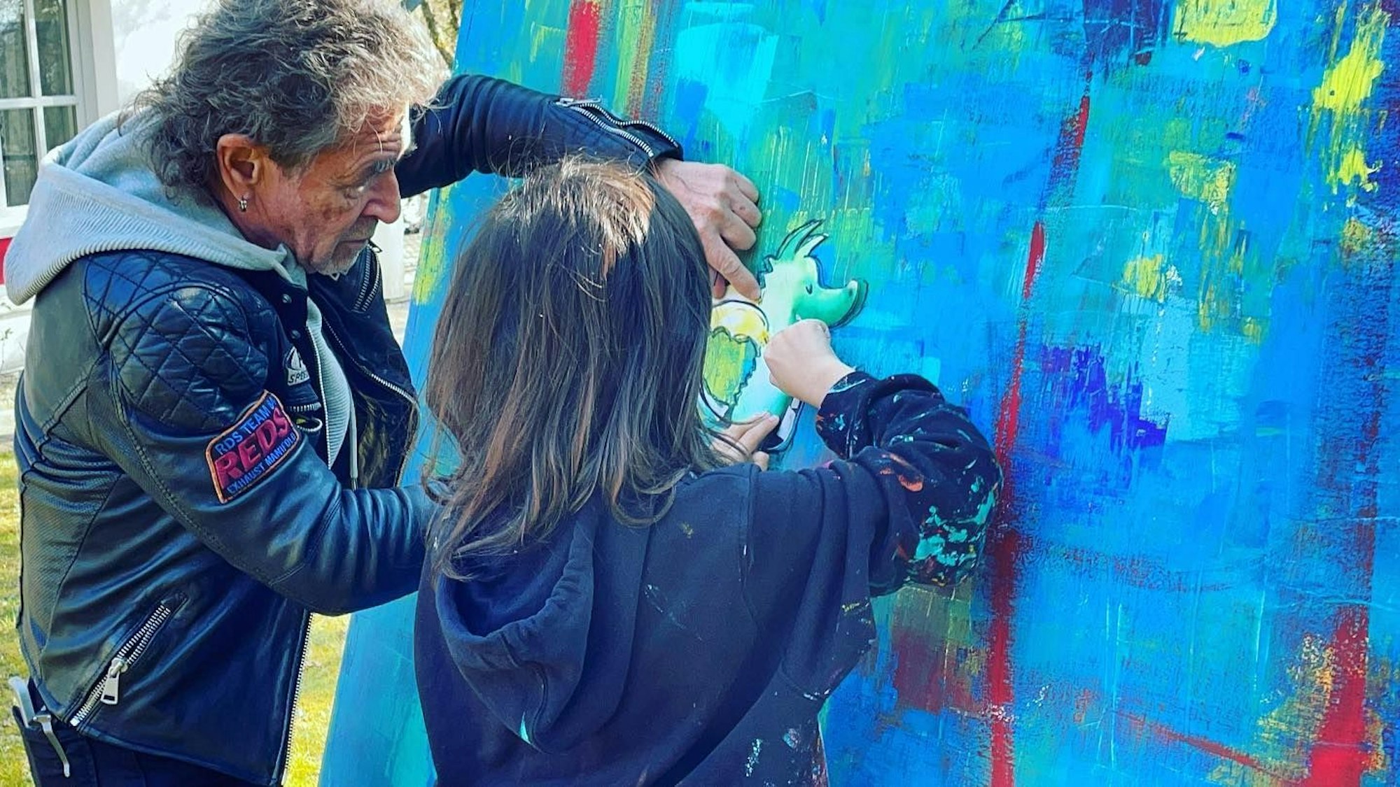 Mikail Akar und Peter Maffay malen ein Gemälde auf einer Leinwand.