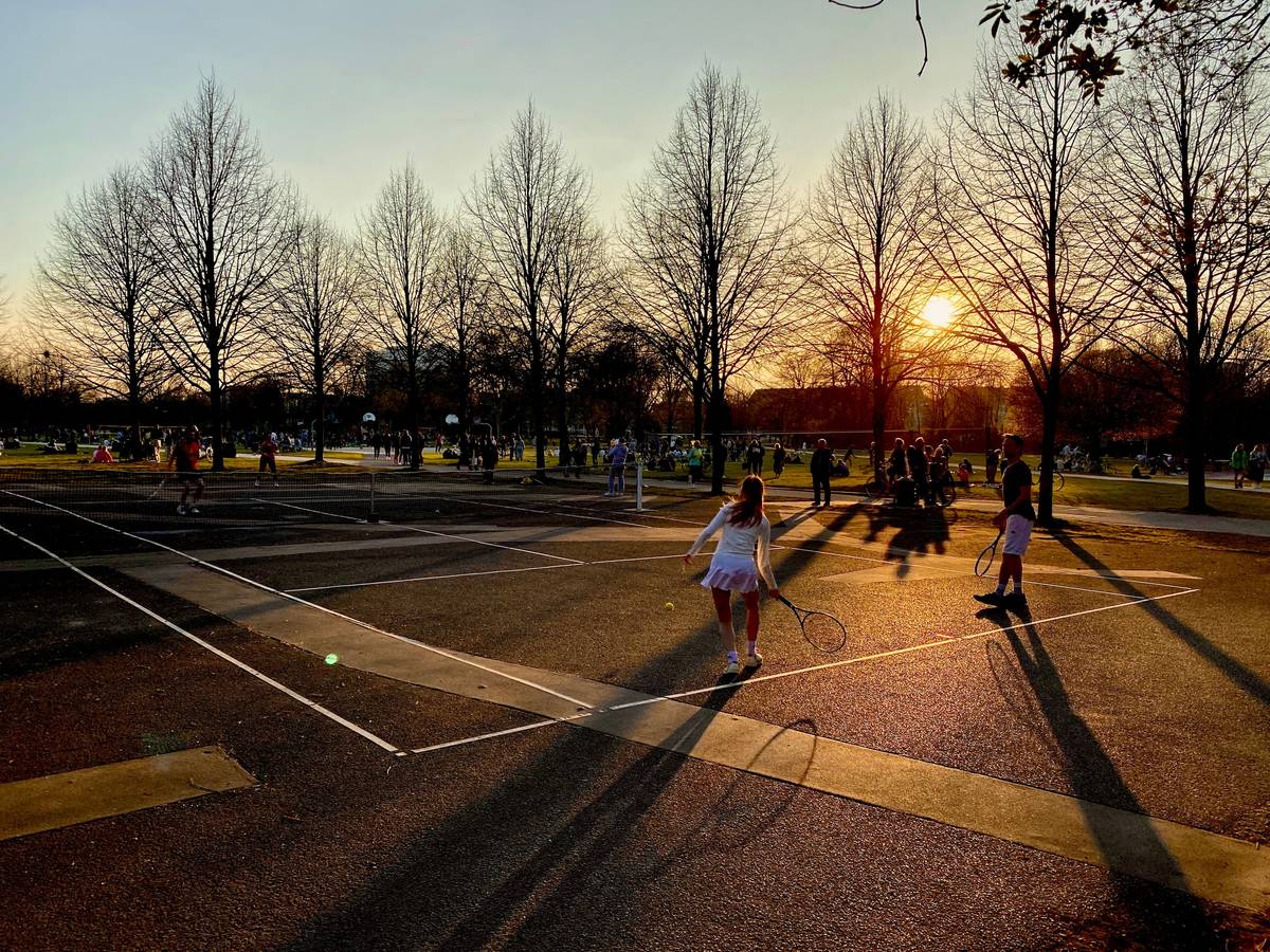 Menschen spielen in der Abendsonne auf einem öffentlichen Tennisplatz.