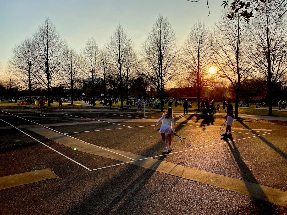 Menschen spielen in der Abendsonne auf einem öffentlichen Tennisplatz.