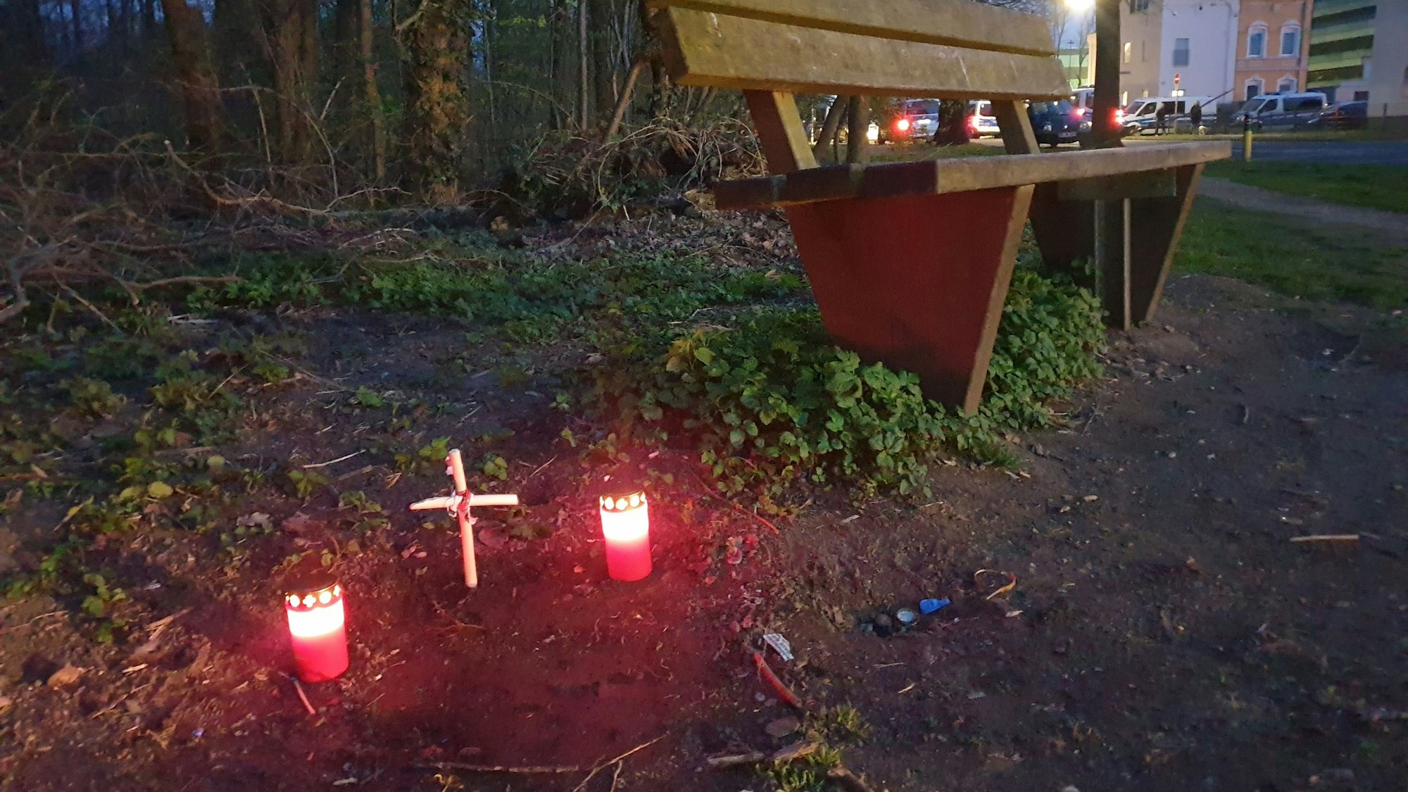Ein Kreuz und zwei Kerzen stehen neben einer Sitzbank.