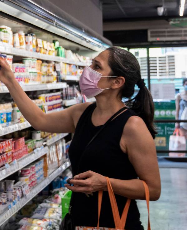 Eine Frau mit Mund-Nasen-Bedeckung steht vor einem Kühlregal im Supermarkt.