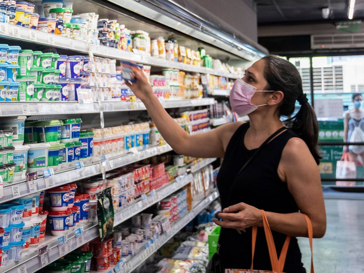 Eine Frau mit Mund-Nasen-Bedeckung steht vor einem Kühlregal im Supermarkt.