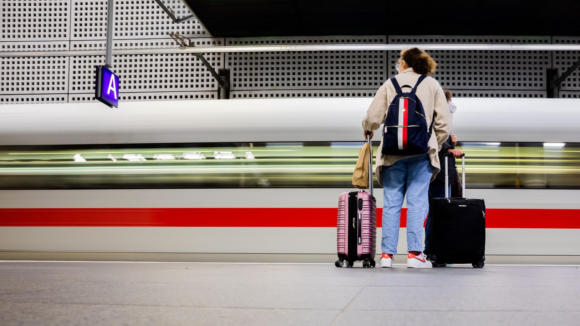 Frau steht mit Koffern an Bahnsteig, ICE fährt durch.