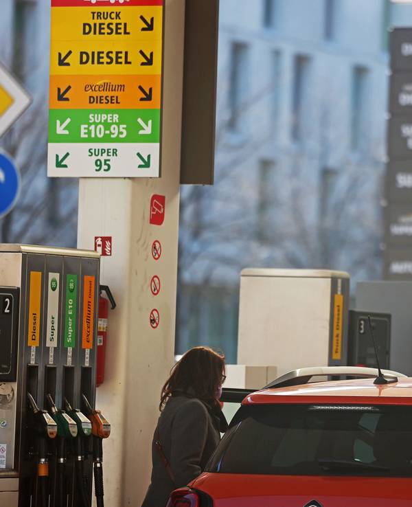 Frau steht mit Auto an einer Tankstelle.