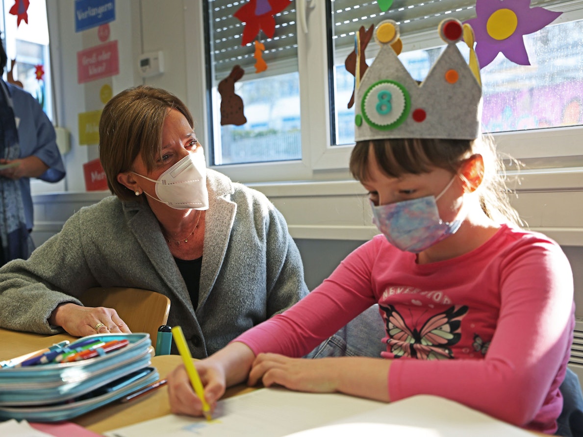 Schulministerin Yvonne Gebauer sitzt mit einem Mädchen in einer Schulklasse am Tisch.