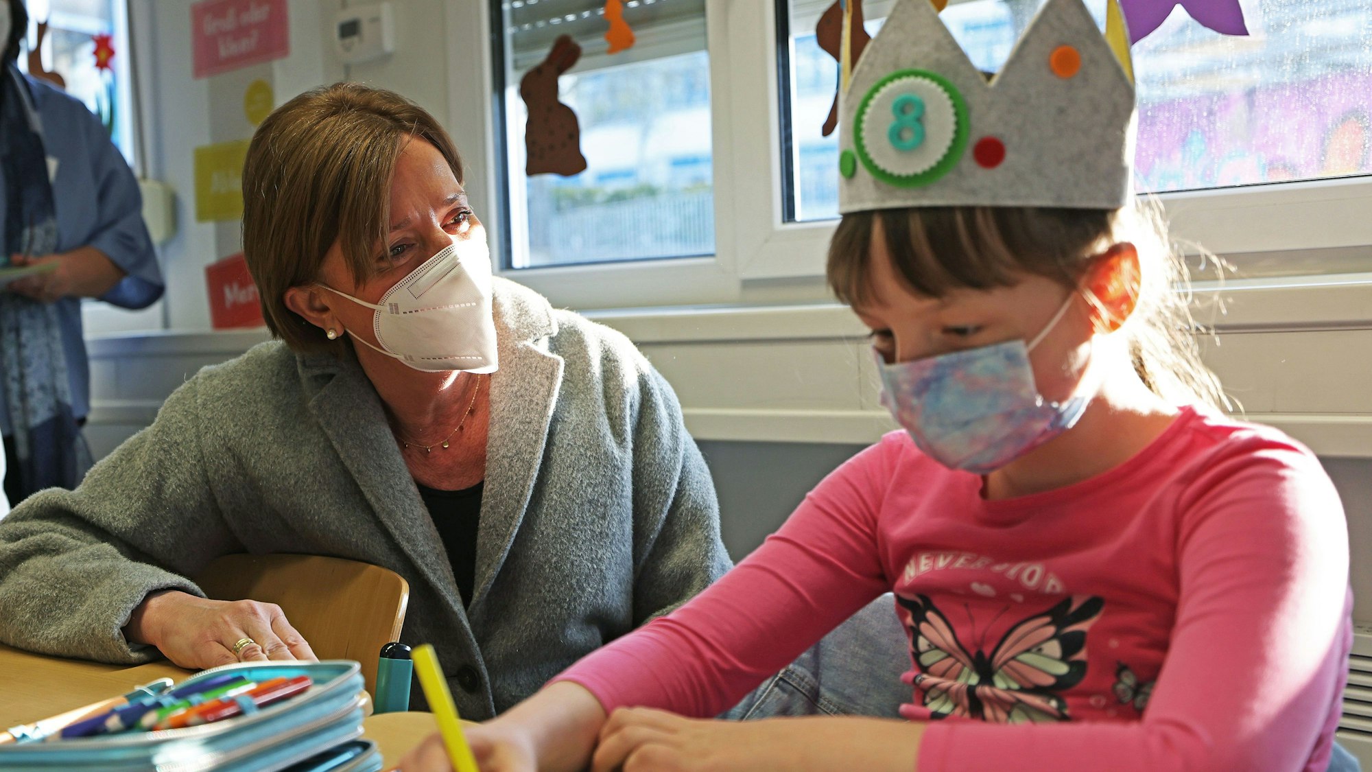 Schulministerin Yvonne Gebauer sitzt mit einem Mädchen in einer Schulklasse am Tisch.