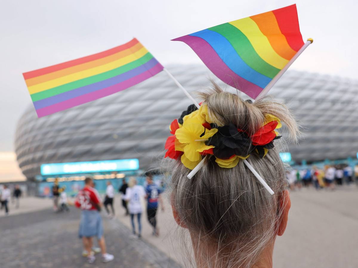 Eine Fußball-Anhängerin mit zwei kleinen Regenbogenfahnen im Haar steht vor der Münchner Allianz-Arena.