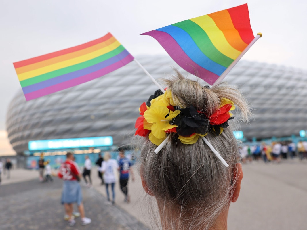 Eine Fußball-Anhängerin mit zwei kleinen Regenbogenfahnen im Haar steht vor der Münchner Allianz-Arena.
