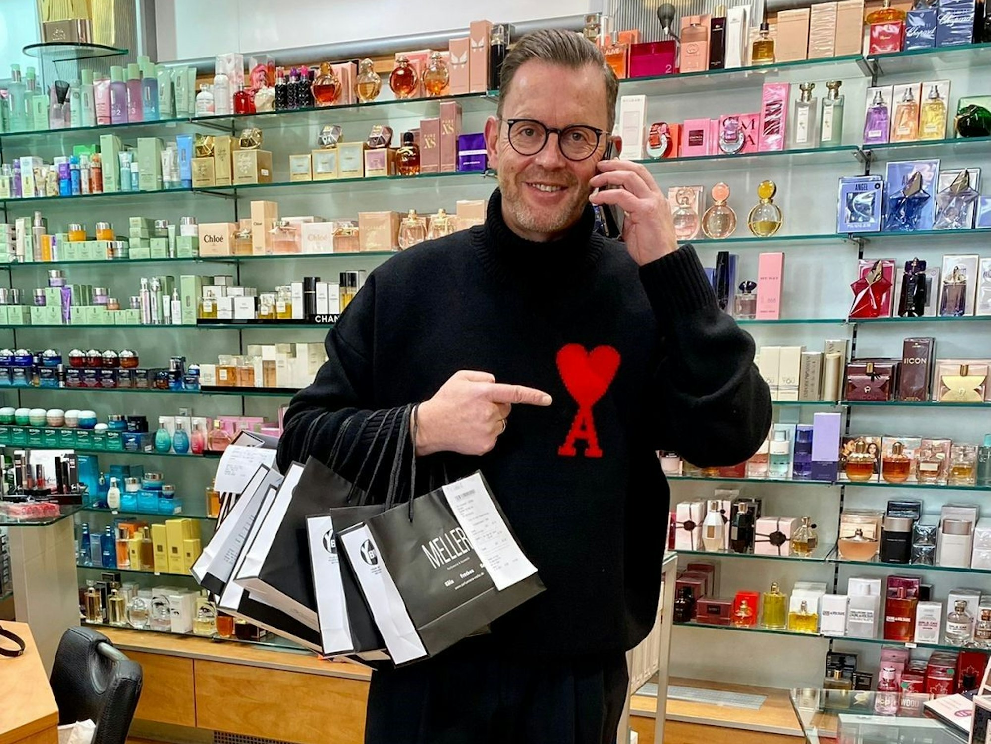 Heinz-Josef Meller steht mit Telefon und Einkaufstüten in seiner Parfümerie Meller in Köln.