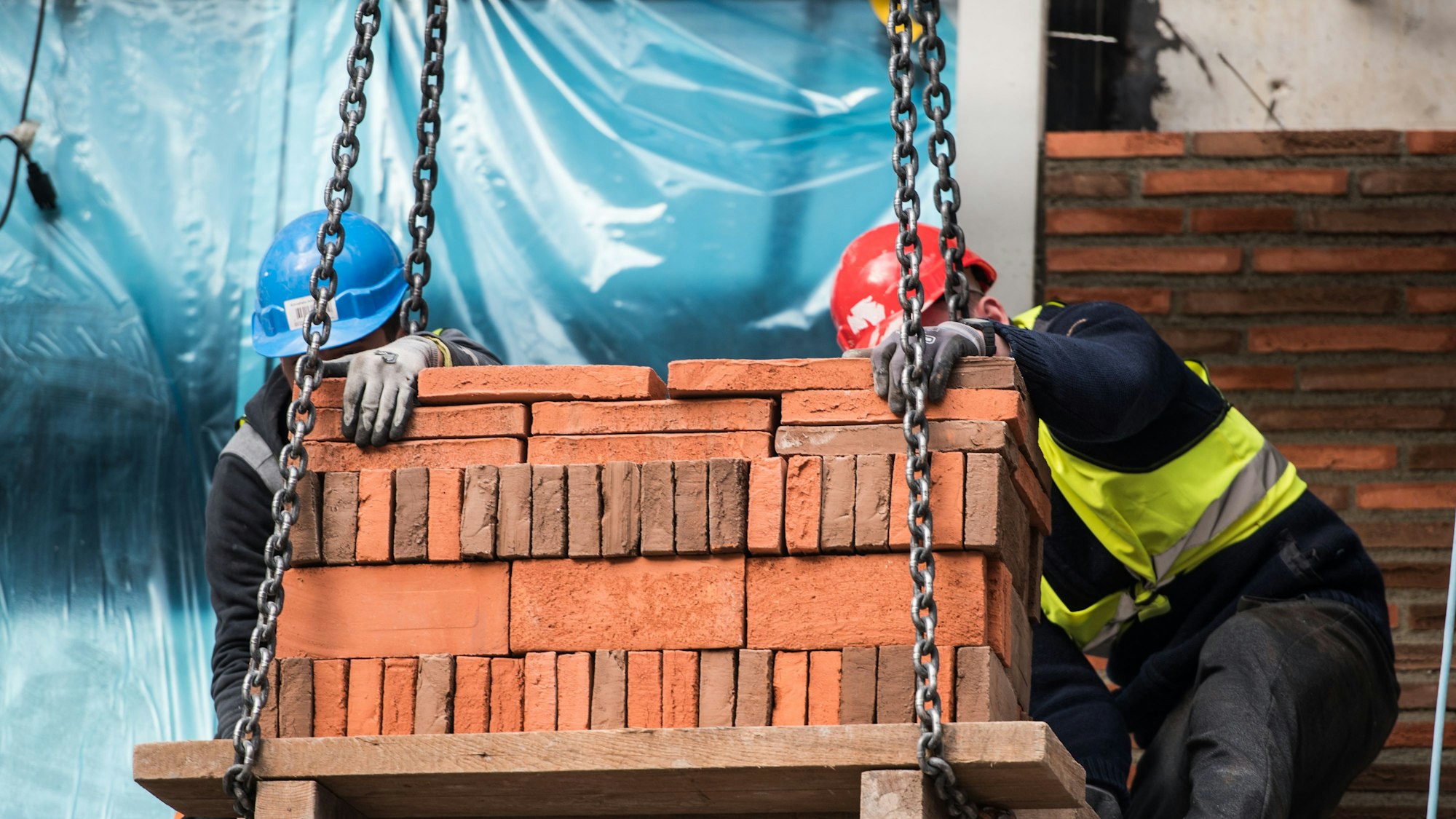 Bauarbeiter setzen eine Palette Backsteine ab.
