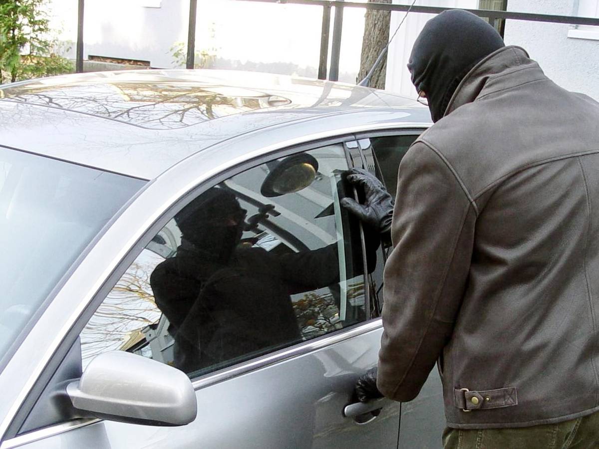 Ein Mann, der sein Gesicht vermummt hat, versucht, ein Auto zu stehlen.